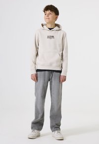 Sudadera color crema con el texto negro "PERSPECTIVA DEL FUTURO", bolsillo tipo canguro; combinada con jeans gris claro y zapatillas blancas.