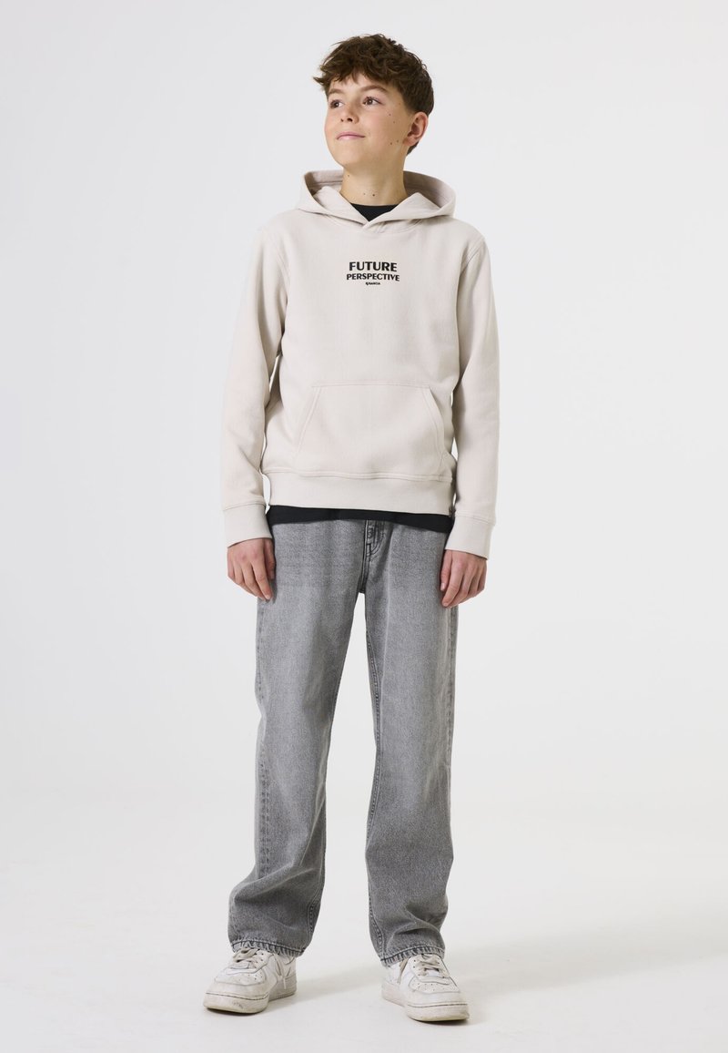 Sudadera color crema con el texto negro "PERSPECTIVA DEL FUTURO", bolsillo tipo canguro; combinada con jeans gris claro y zapatillas blancas.