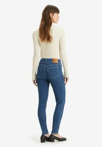 Jeans ajustados de mezclilla azul, con dos bolsillos traseros, una etiqueta de cuero en la cintura, combinados con una blusa de manga larga de canalé color crema.