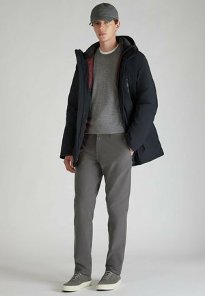 Chaqueta acolchada negra con capucha, suéter gris de cuello redondo, pantalones gris claros y gorra gris. Los zapatos son ligeros y de una tela texturizada.