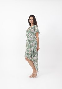 Vestito verde floreale con maniche corte a sbuffo, scollo a V, vita cintrata e orlo asimmetrico. Decorato con fiori rosa chiaro e bianchi.