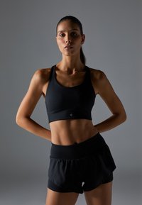 Svart sports-bh og matchende høyt liv shorts, laget av elastisk stoff, med en tettsittende design og minimalistisk logo-detall.