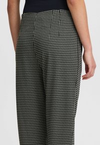 Pantalon en noir et blanc à motif pied-de-poule avec taille haute et coupe droite, présentant un tissu texturé et une couture arrière élégante.