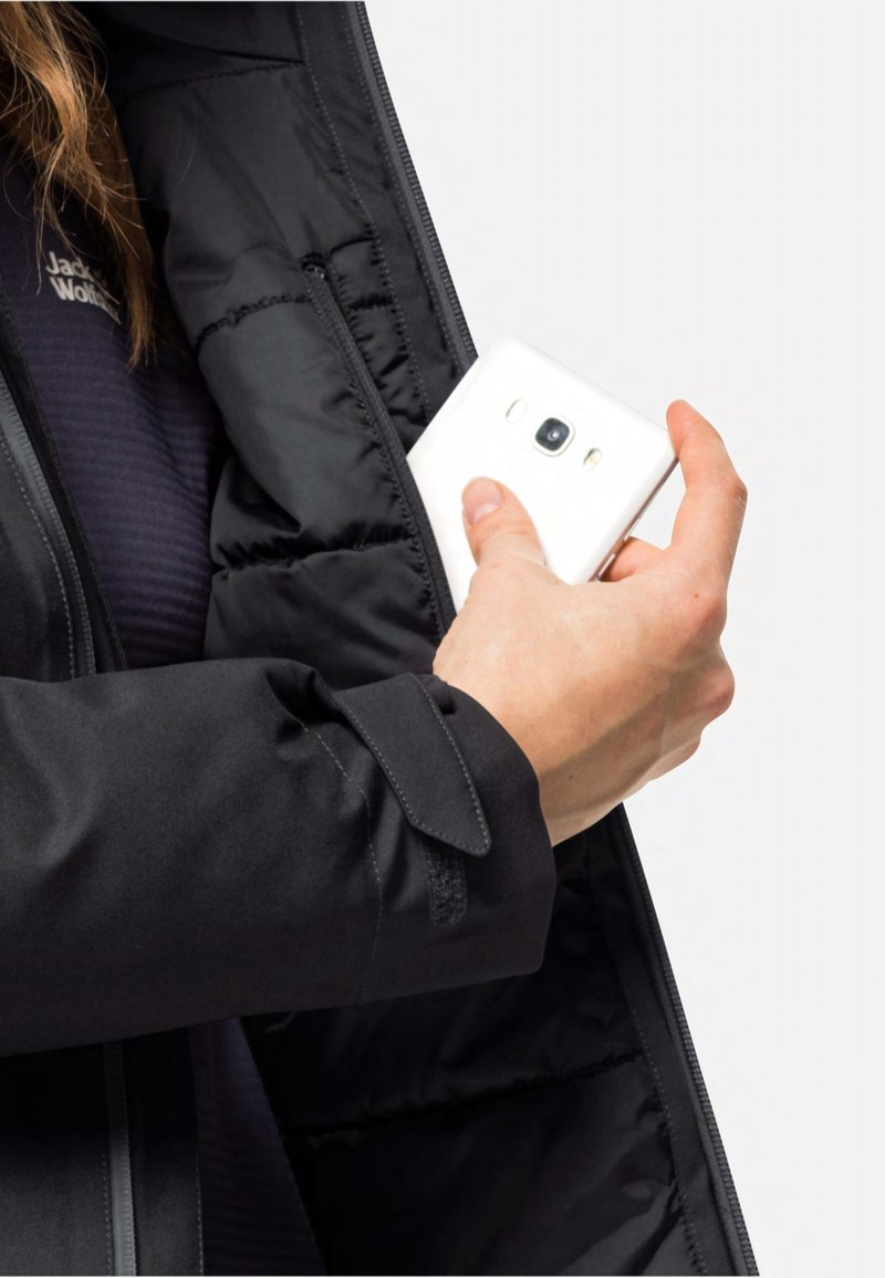 Schwarze Pufferjacke mit einem Reißverschluss, in der eine Hand ein weißes Smartphone aus der Innentasche greift.