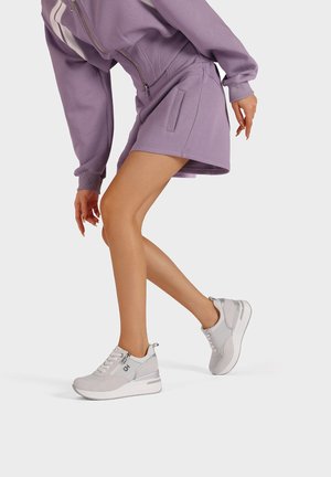 Scarpe da ginnastica grigie realizzate in rete e suede, con zip e suola arrotondata, abbinate a una gonna larghi lilla e a una felpa.