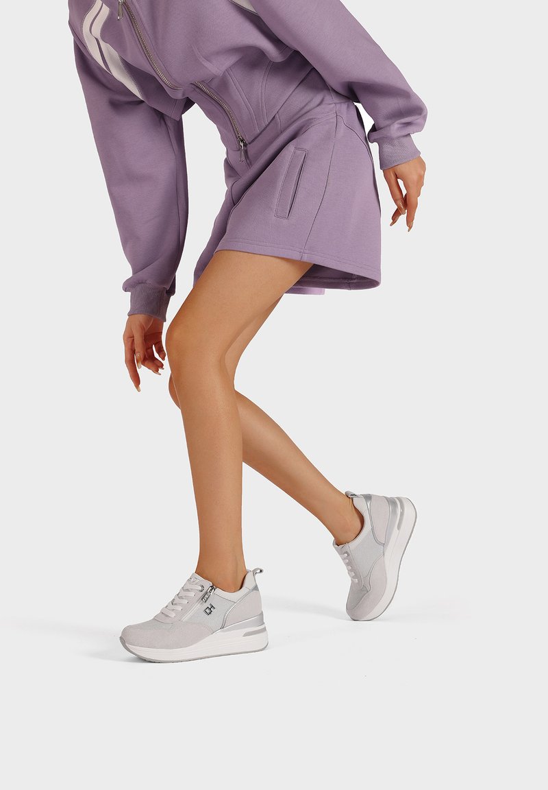 Scarpe da ginnastica grigie realizzate in rete e suede, con zip e suola arrotondata, abbinate a una gonna larghi lilla e a una felpa.