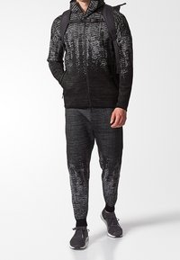 Black athletic tracksuit with a textured pattern, featuring a zip-up hoodie and joggers, complemented by a backpack and running shoes.