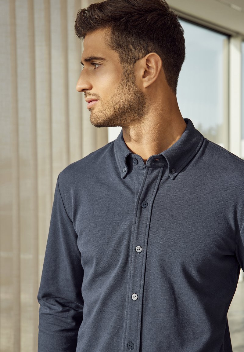 Dunkelblauses Langarmshirt mit Kragen zum Knöpfen, aus glattem Stoff, mit einer Vorderleiste und kontrastierenden Knöpfen sowie einer taillierten Passform.
