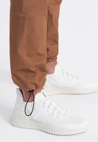 Witte sportieve sneakers met een textuur van mesh en gevoerde zolen, in combinatie met losvallende, bruine tapered broek met verstelbare enkel-details.