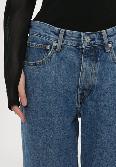 Ανοιχτό μπλε τζιν παντελόνι με ψηλή μέση, φερμουάρ και πέντε τσέπες. Διαθέτει αντίθεση στη ραφή και ελαφρώς ξεθωριασμένη υφή.