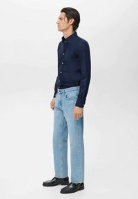 Camicia blu navy con bottoni abbinata a jeans a gamba dritta azzurri e scarpe nere. Tessuto morbido, vestibilità su misura e elementi di design classici.