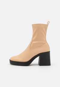 Beige ankle boot made of smooth material with a rounded toe, elastic side, and a chunky black block heel. Features a pull tab at the back.