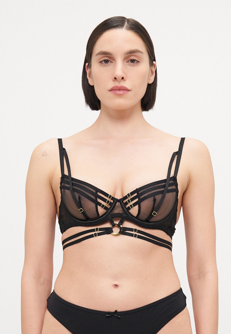 Soutien-gorge en mesh noir avec des bonnets structurés, présentant des accents en métal doré et plusieurs bretelles réglables pour un ajustement parfait. Détail en tissu texturé.