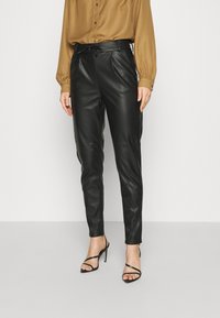 Svarta läderbyxor med en elegant design, featuring en bältad midja, raka ben och sidofickor. Kombination med en brun blus och svarta klackar.