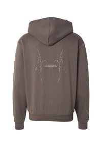 Brown hoodie with spiked tribal design and text "The Originator of Streetwear Since 1989" on the back, featuring ribbed cuffs and hem.