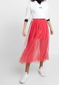 Röd tüll midi kjol med genomskinliga lager, med vita sidoband. Kombinerad med en kortärmad vit sweatshirt och vita sneakers.