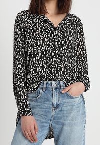 Blůza s černobílým vzorem a límečkem, s knoflíkovým zapínáním vpředu a dlouhými rukávy, spárovaná s světle modrými džíny s vysokým pasem.