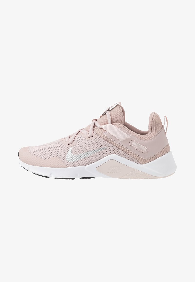 Jasnoróżowy but sportowy z siateczkową cholewką, teksturowanymi nakładkami i białą podeszwą. Posiada wyściełany kołnierz i elementy odblaskowe. Logo Nike obecne.