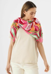 Kleurige sjaal met een patroon in roze, oranje en groene tinten. Lichtgewicht stof met een franjerand, casual gedragen over een crèmekleurig topje.