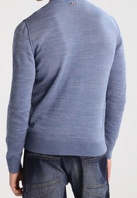 Maglione blu lavorato a maglia con una finitura testurizzata, collo rotondo e polsini e orlo a coste. Presenta un piccolo accento a righe sulla parte posteriore del collo.