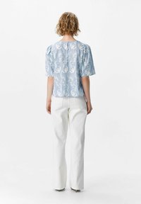Blusa azul claro con bordado floral blanco, mangas cortas abullonadas y escote redondo, combinada con pantalones anchos blancos.