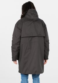 Parka gris foncé avec capuche et dos superposé. Fait en un matériau résistant à l'eau, avec une coupe ample et des poches latérales.