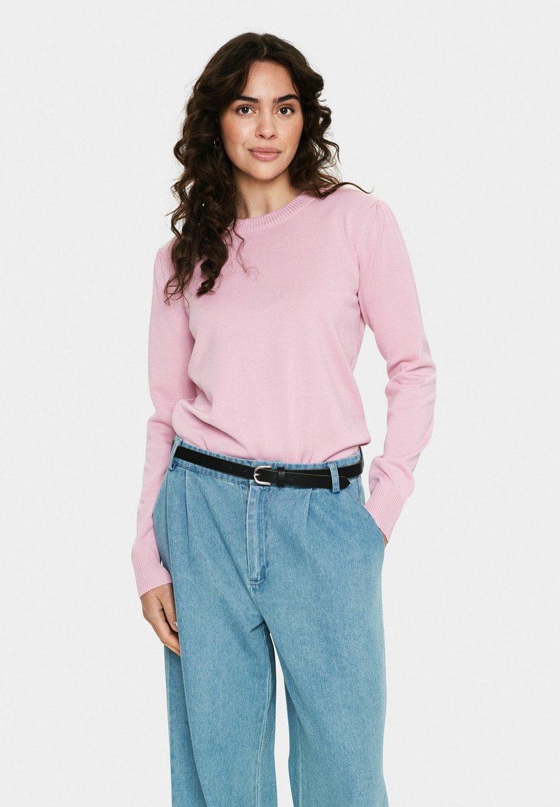 Pull rose clair à manches longues avec col côtelé, associé à un pantalon en denim bleu clair à coupe décontractée et une ceinture noire.