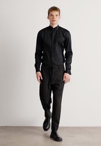 Svart collared skjorte med frontknapper, kombinert med svarte bukser. Strømlinjeformet stoff og skreddersydd passform, brukt med svarte ankelstøvler.