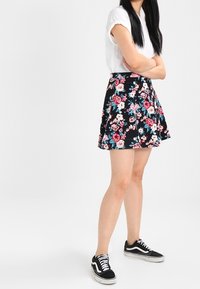 Jupe patineuse fleurie noire avec des fleurs roses et bleues, en tissu léger, associée à un haut blanc et des baskets noires.