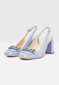 Talons slingbacks en cuir verni bleu clair avec un talon bloc épais et un accent décoratif en chaîne argentée sur le bout. Texture lisse.