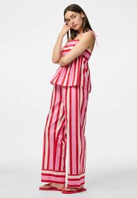 Ensemble deux pièces à rayures verticales rouges et roses, comprenant un top peplum sans manches et un pantalon à jambes larges. Tissu en coton doux et des tongs assorties.
