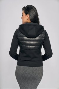 Kvinde set bagfra iført en sort hættejakke med polstret ryg og en sølvgrå, ribstrikket nederdel.