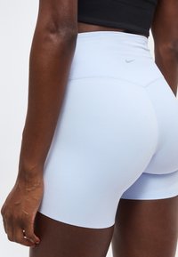 Gros plan sur une personne portant un short de sport taille haute Nike bleu clair et un top court noir, montrant le dos et le côté.