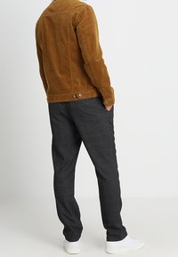 Brun fløjlskjorte med bagknapper, parret med grå strikkede bukser og hvide sneakers. Stof med synlig ribb.