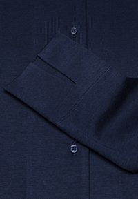 Marineblauwe knopsluiting overhemd met een zachte textuur, voorzien van een enkele knoopsluiting en opgerolde mouwdetails.