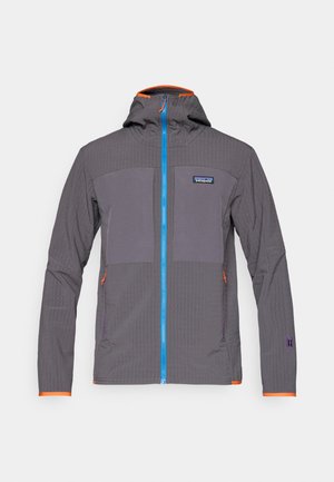 Grå lett jakke med hette, med en blå glidelås, oransje detaljer og distinkte teksturerte paneler på fronten og ermene.