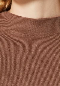 Brauner, gerippter Pulloverstoff mit hohem Kragen. Die Textur ist weich mit einem einheitlichen Muster aus vertikalen Linien, das das Strickdesign betont.