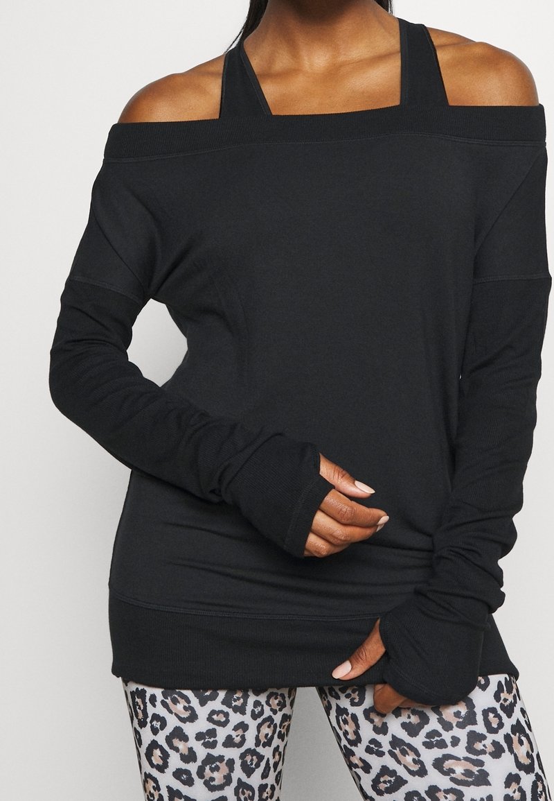 Haut noir à manches longues et épaules dénudées avec des passants pour les pouces, doté de poignets côtelés et d'une coupe décontractée, associé à des leggings imprimés léopard.