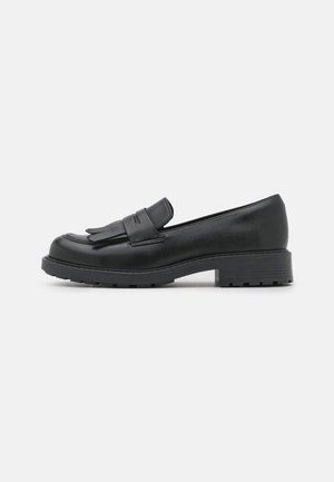 Mocassin en cuir noir avec semelle et talon épais, doté d'un détail à franges avec pampilles sur le dessus, présenté en vue latérale sur fond blanc.