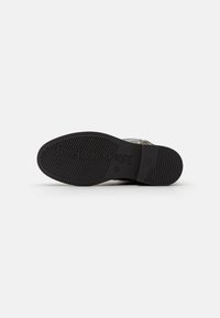 Sole in gomma nera con texture rigata e logo inciso; design piatto adatto a vari stili di calzature. Materiale superiore liscio non visibile.
