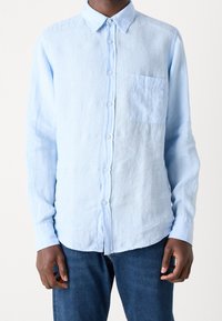 Camicia di lino azzurra chiara a maniche lunghe con colletto a bottoni, tasca frontale e chiusura con bottoni; tessuto testurizzato con vestibilità casual.