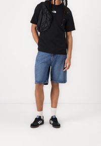 Black t-shirt with a white logo, blue denim shorts, black sneakers with white stripes, and light socks. Casual streetwear style.