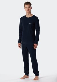 Marineblauw katoenen pyjama-top met lange mouwen, een borstzak en witte accenten, gecombineerd met bijpassende broek, met een ontspannen pasvorm en elastische manchetten.