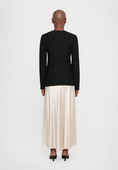 Black textured long-sleeve top with a rectangular pattern, paired with a flowing cream satin maxi skirt and black pointed toe heels.
