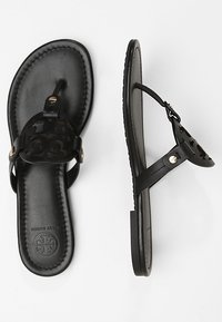 Tongs en cuir noir avec une semelle texturée, un design découpé sur la sangle et des accents en métal doré.