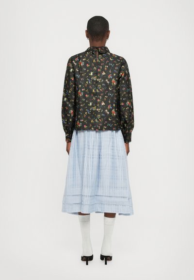 Blusa nera floreale con maniche a sbuffo, abbinata a una gonna plissettata blu chiaro. Presenta una chiusura sul collo posteriore e tessuti testurizzati.