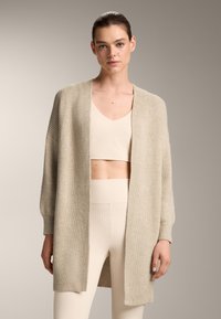 Béžový rebrovaný cardigan s otvoreným predným dielom, vo voľnom strihu a s dlhými rukávmi. Nosený cez zodpovedajúci skrátený top a legíny s vysokým pásom.