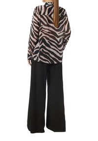 Transparent button-up blouse with zebra print in shades of black and pink, paired with wide-leg black trousers. Long sleeves and back pleat detail.