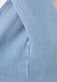 Tissu en denim bleu clair avec une couture visible qui croise à un léger angle, montrant la texture et les détails du tissage.