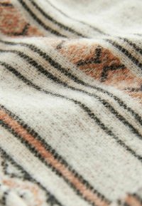 Tissu en laine douce avec des motifs géométriques et des rayures beige, noir et rouille, présenté en gros plan avec des plis délicats.